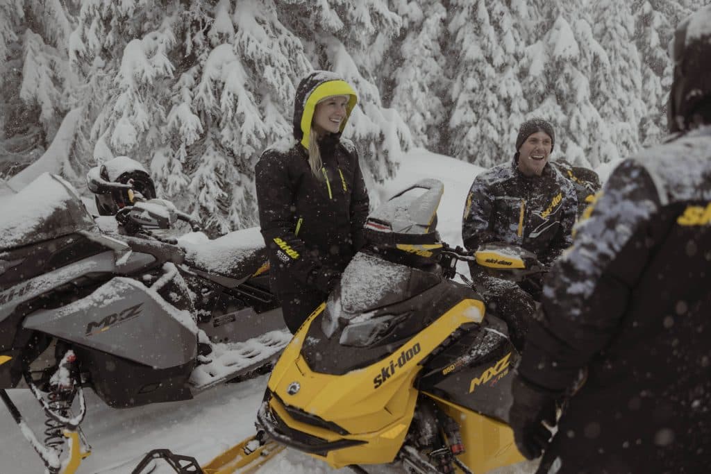 trois personnes assises en rond sur leurs motoneiges ski-doo 2025 discutent