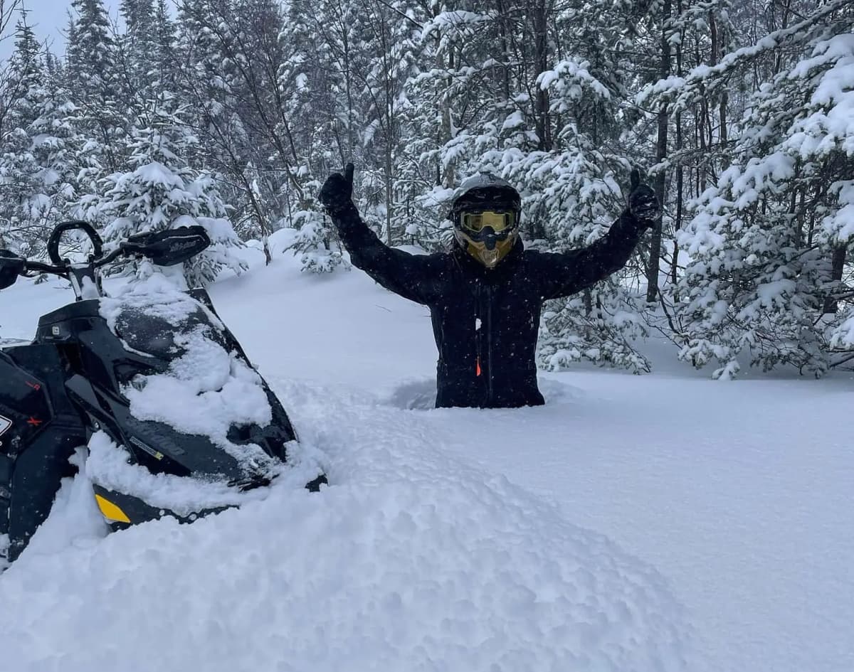 Andrew Ranger dans la neige jusqu'aux hanches à côté de sa motoneige