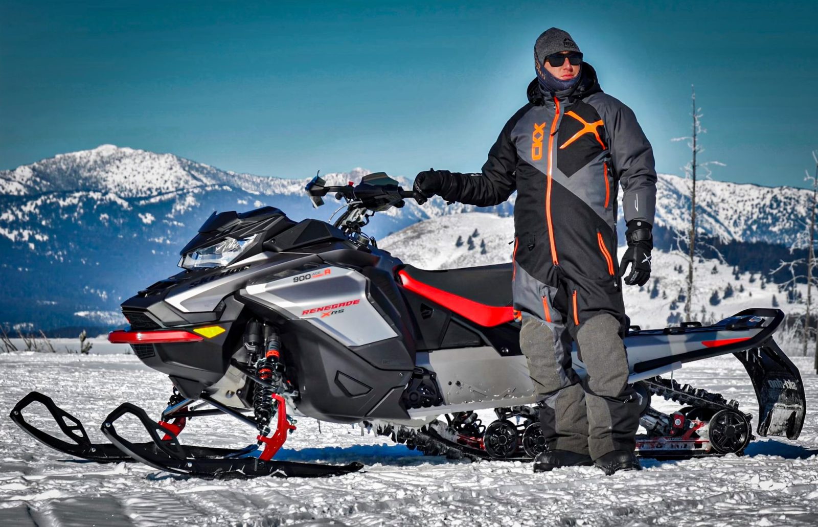 a person wearing the ckx elevation mono-suit standing in front of a snowmobile