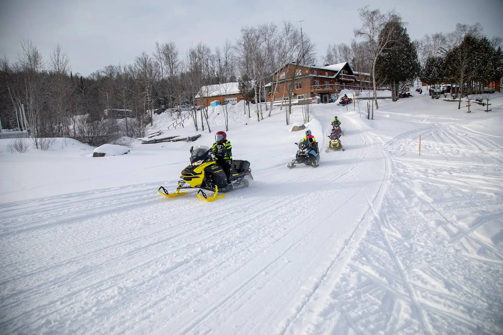 A group of snowmobilers ride on a snow-covered trail near a wooden cabin in the Laurentians, an area recognized as one of the best destinations for snowmobiling.