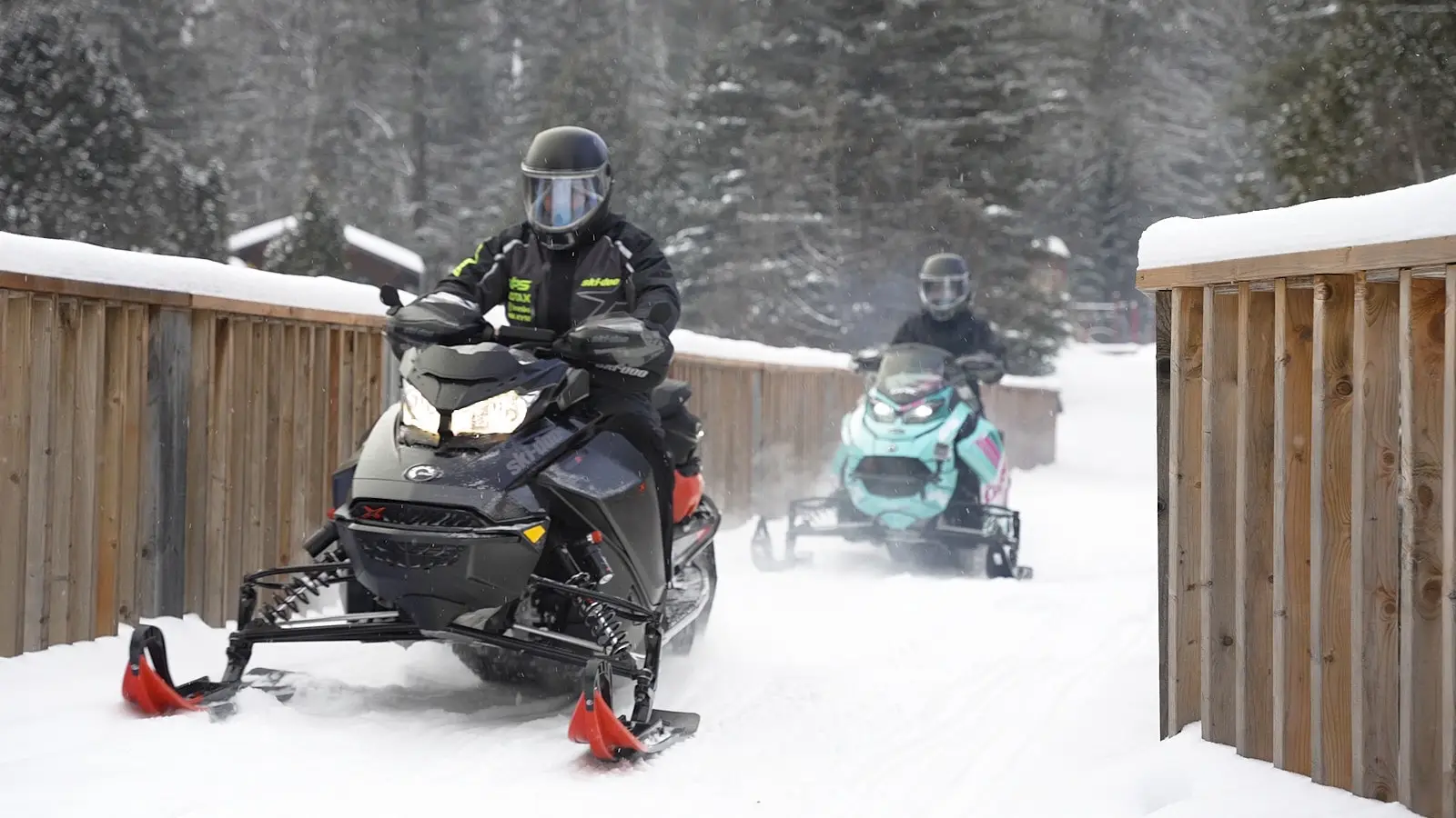 Two snowmobilers crossing a wooden bridge on a snowy trail in Lanaudière-Mauricie, surrounded by winter trees.