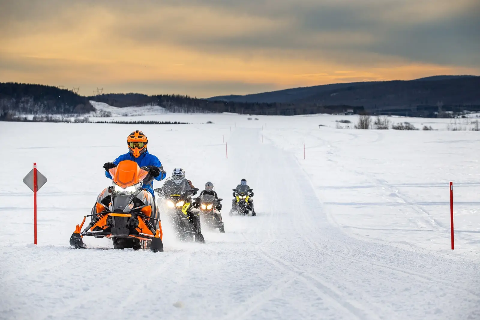 A group of snowmobilers traversing a vast snowy landscape at sunset in Snowmobile Country, Lanaudière-Mauricie