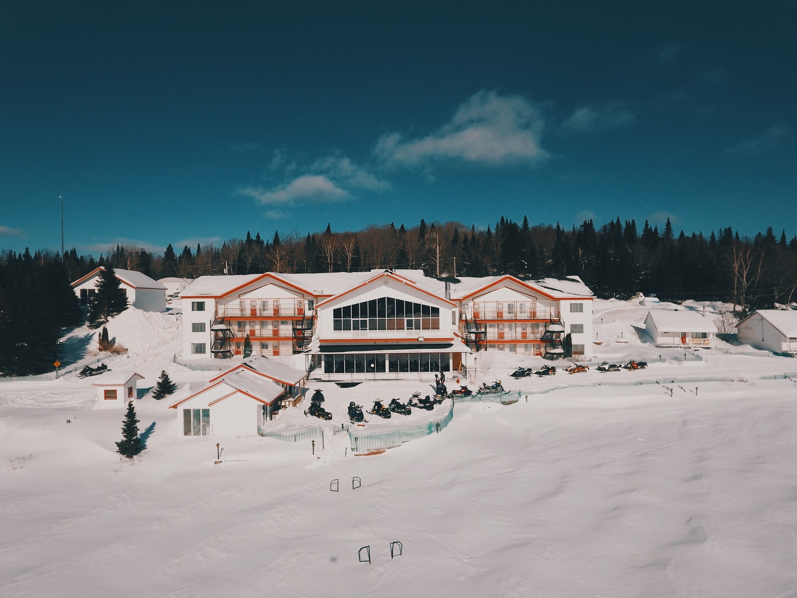 La pourvoirie Au Pays de Réal Massé en Lanaudière, entourée de neige avec des motoneiges stationnées devant le bâtiment principal.