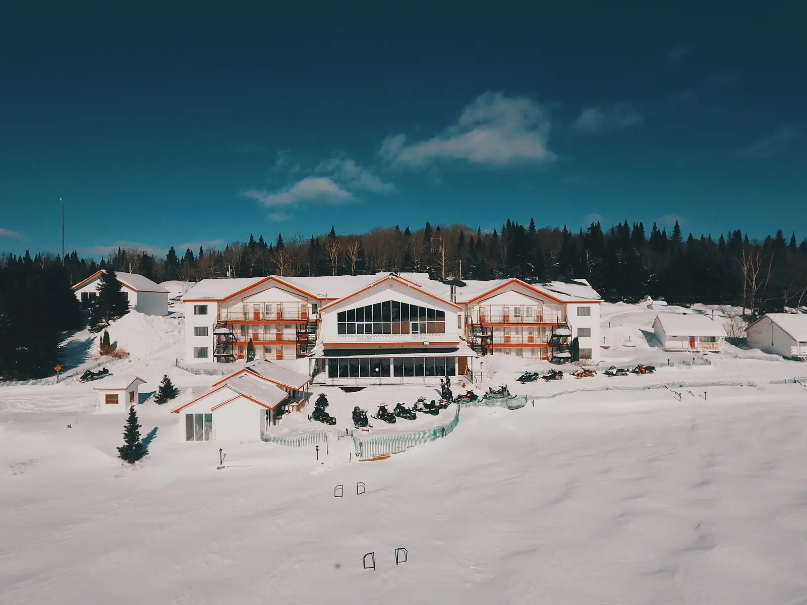 Lodge of Pourvoirie Au Pays de Réal Massé in Lanaudière surrounded by snow with snowmobiles parked in front of the main building.