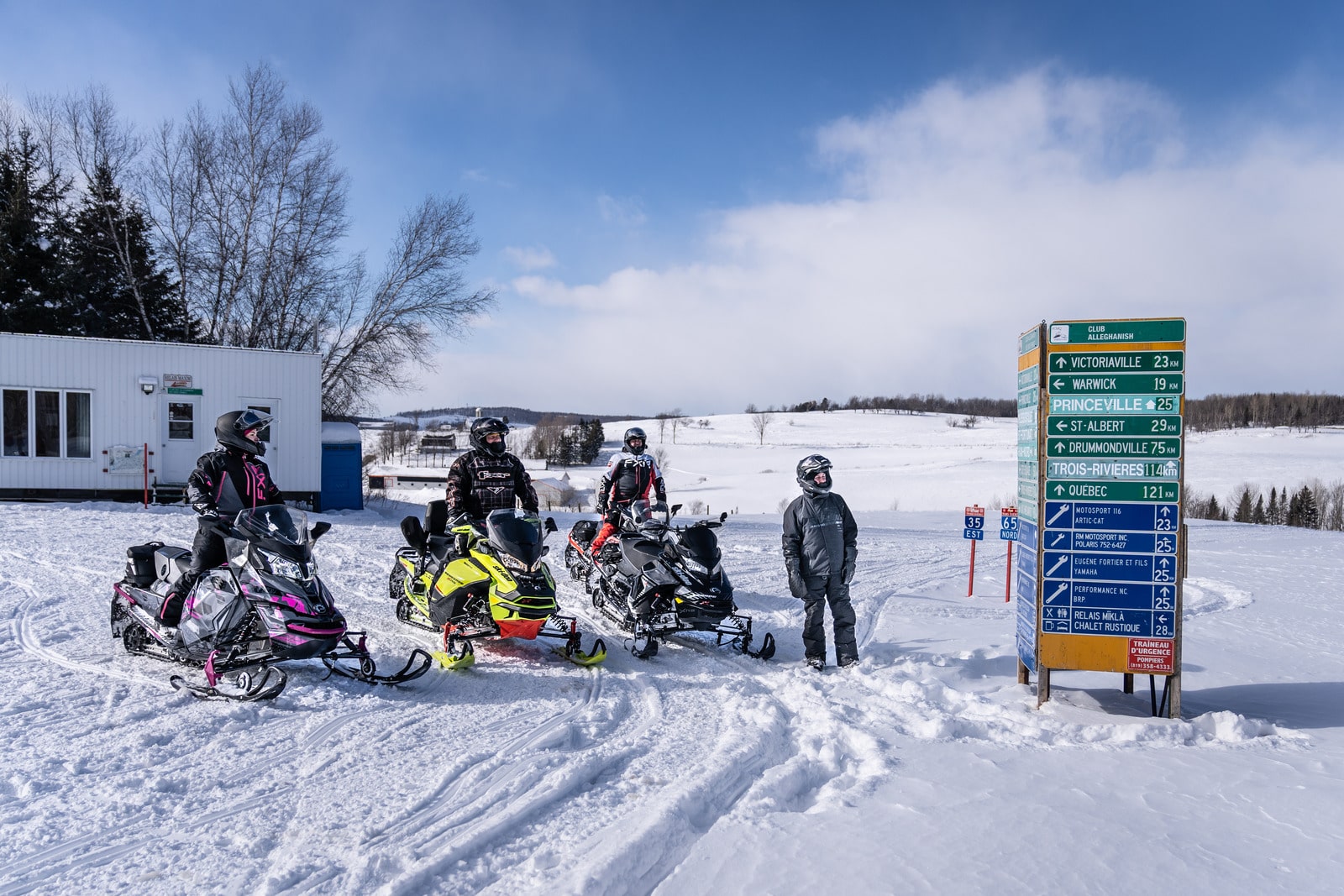 Groupe de motoneigistes arrêtés près d'un panneau directionnel sur les sentiers de motoneige au Québec.