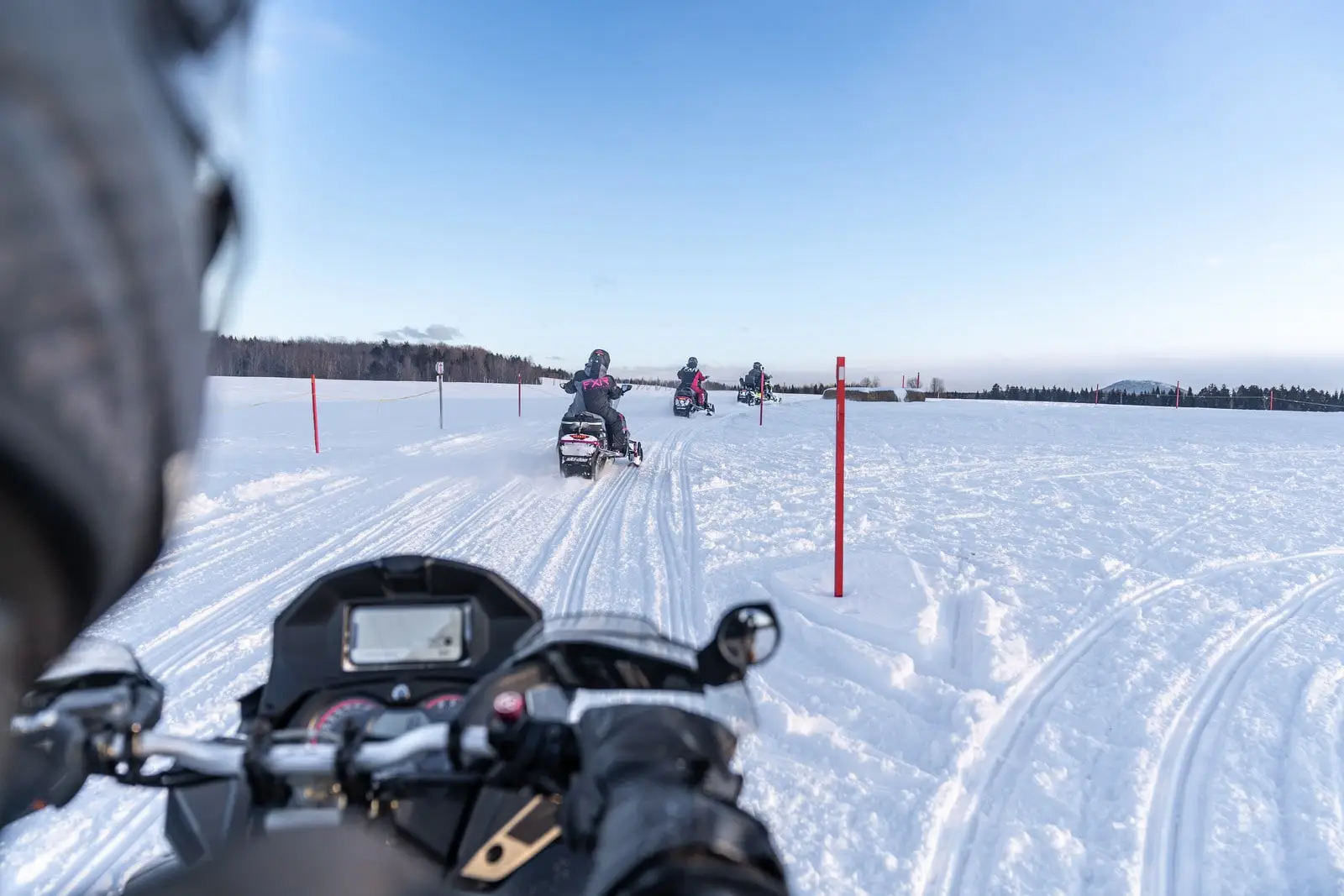 Vue en première personne d'un groupe de motoneigistes roulant sur un sentier enneigé au Québec.