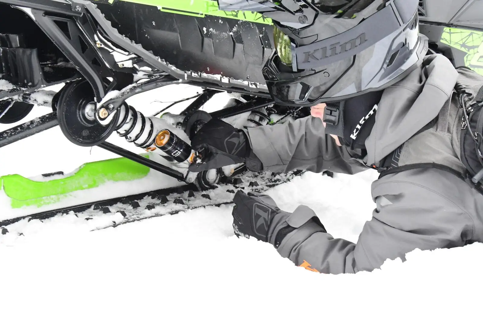 Person inspecting the AC5S suspension system on an Arctic Cat snowmobile in the snow.