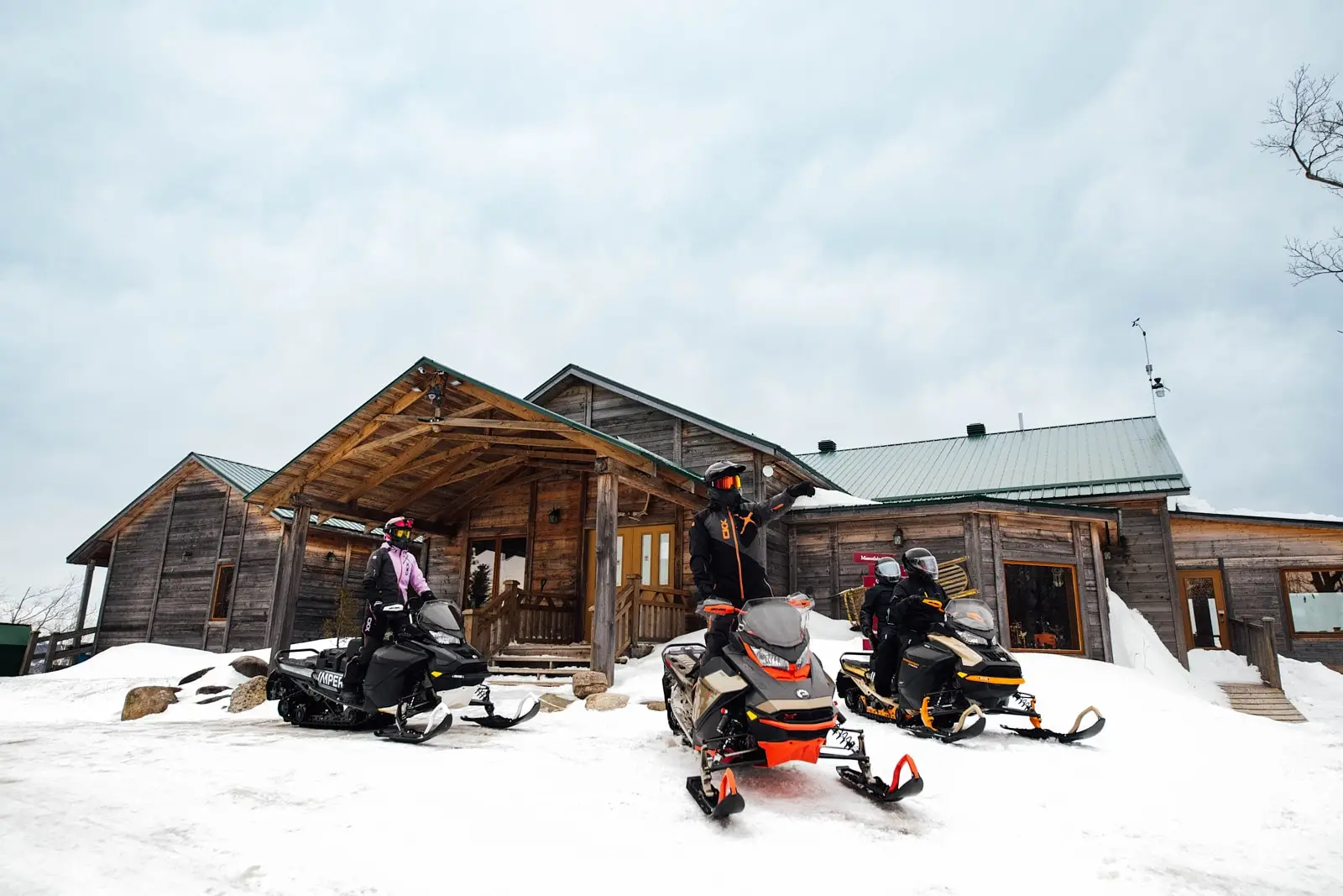 A group of snowmobilers riding through a snowy forest with tall pine trees towering above.