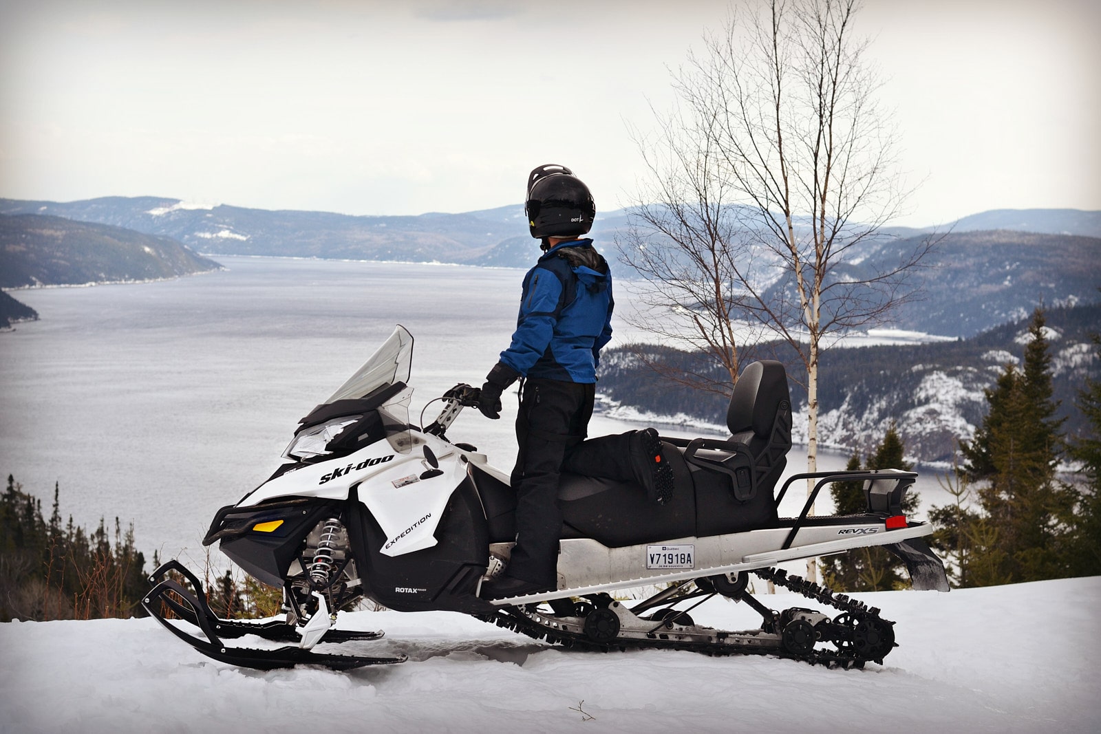 Motoneigiste admirant le fjord enneigé du Saguenay, un incontournable de la saison motoneige au Saguenay–Lac-Saint-Jean.