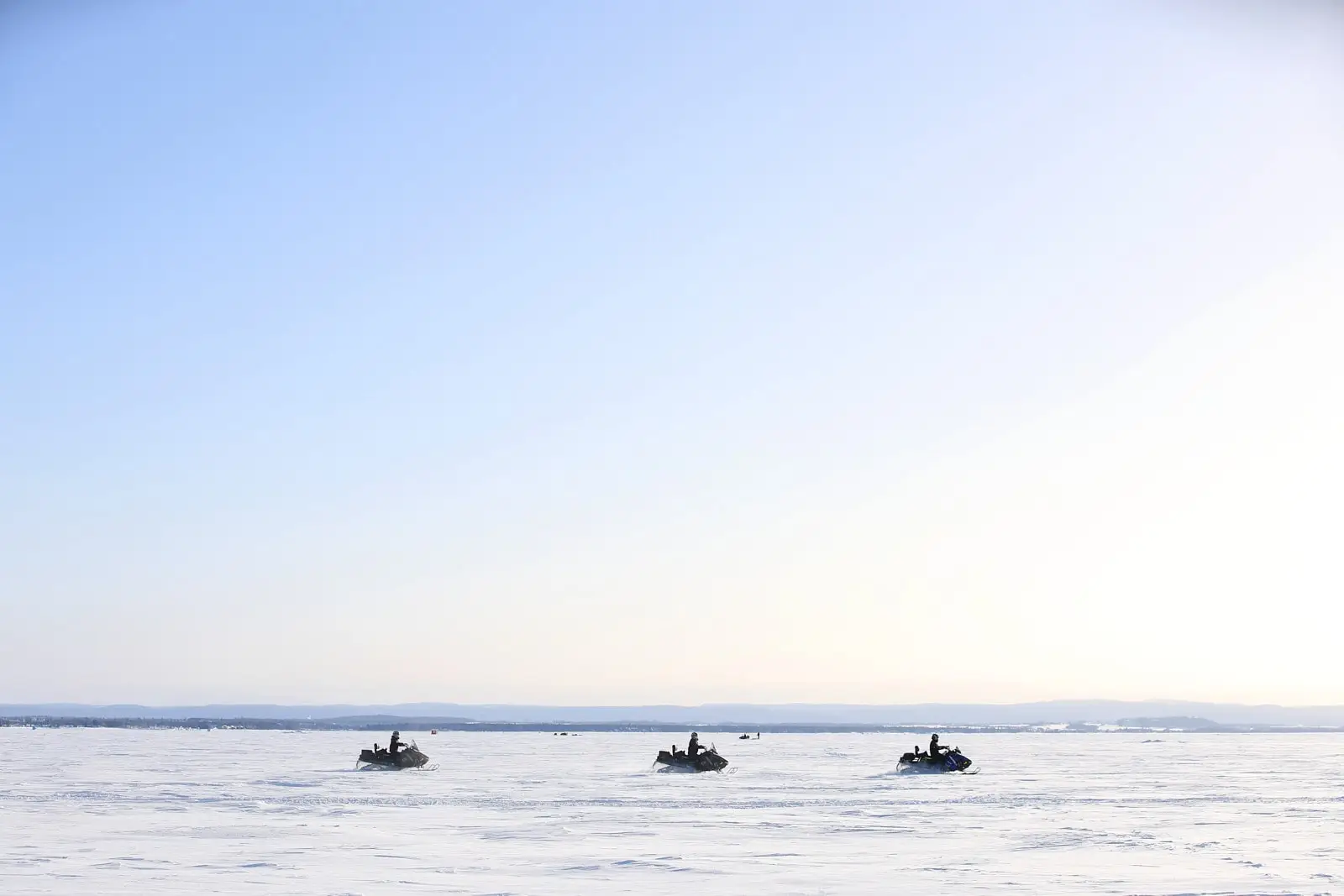 Trois motoneiges en ligne sur une vaste étendue gelée, typique du Tour Lac Saint-Jean en saison motoneige.