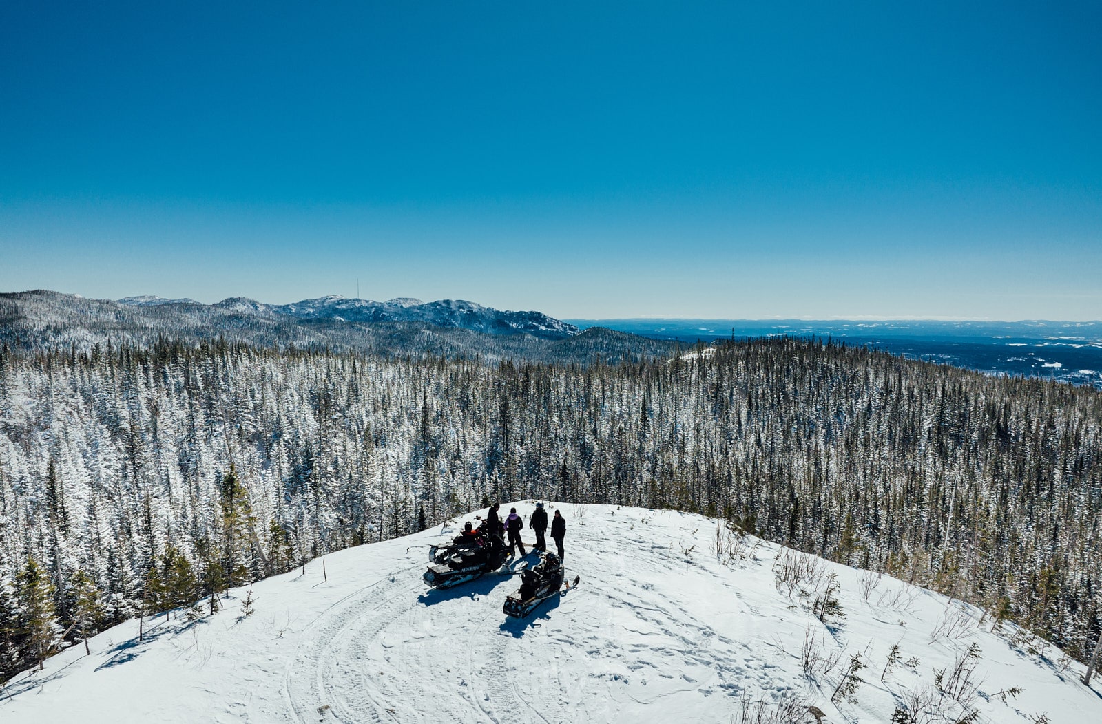 Groupe de motoneigistes au sommet d’une colline enneigée avec vue sur les montagnes du Saguenay–Lac-Saint-Jean.