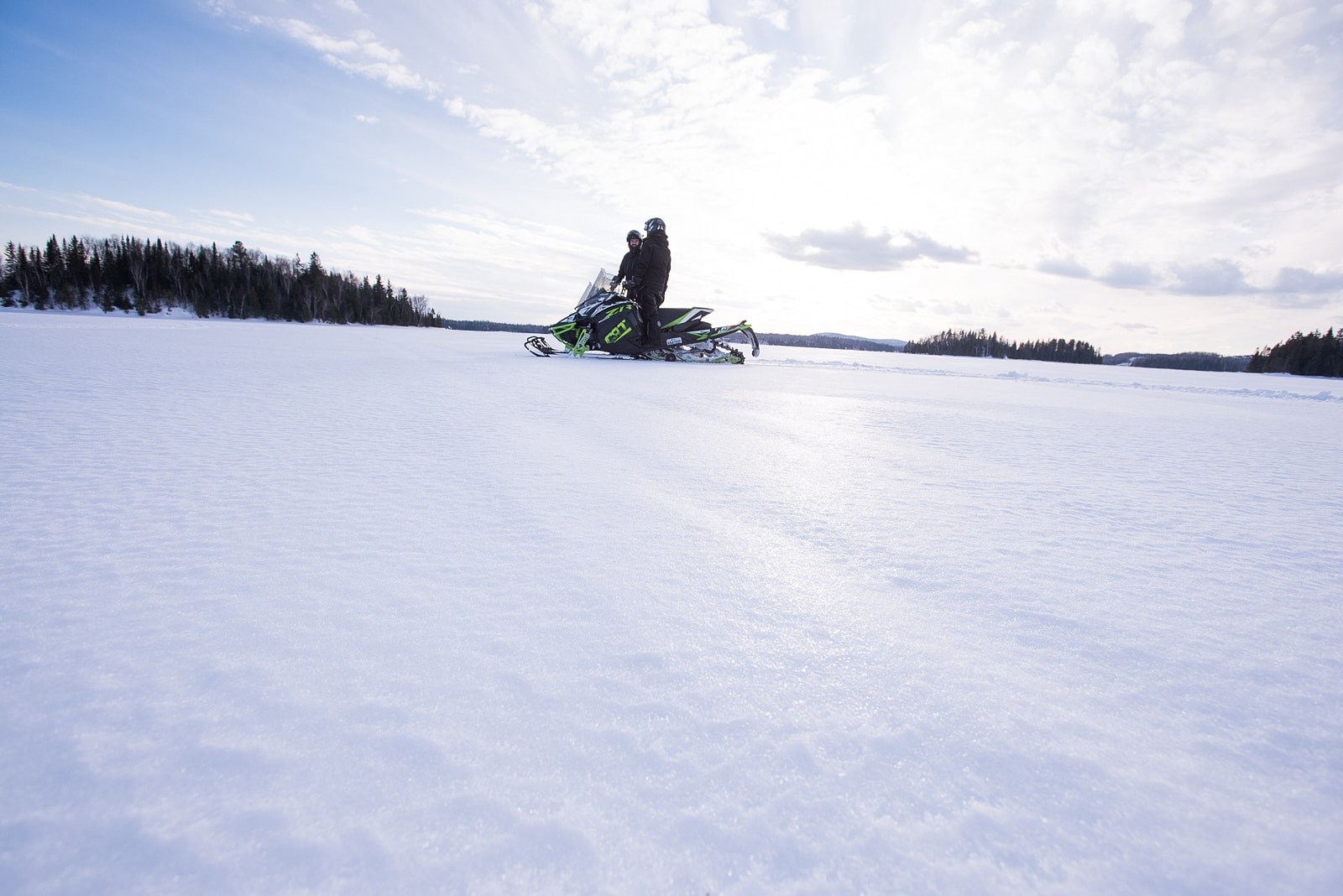 Deux motoneigistes traversant un lac gelé en Abitibi-Témiscamingue sur des sentiers enneigés.