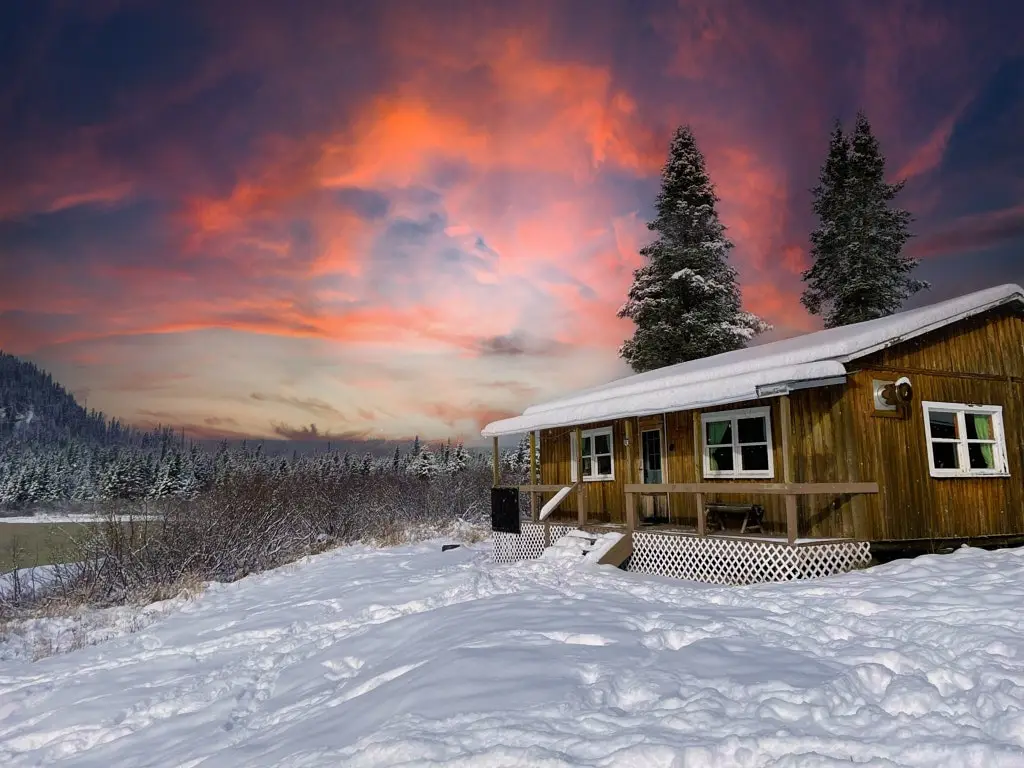 Snow-covered chalet surrounded by forest, illuminated by a beautiful sunset.