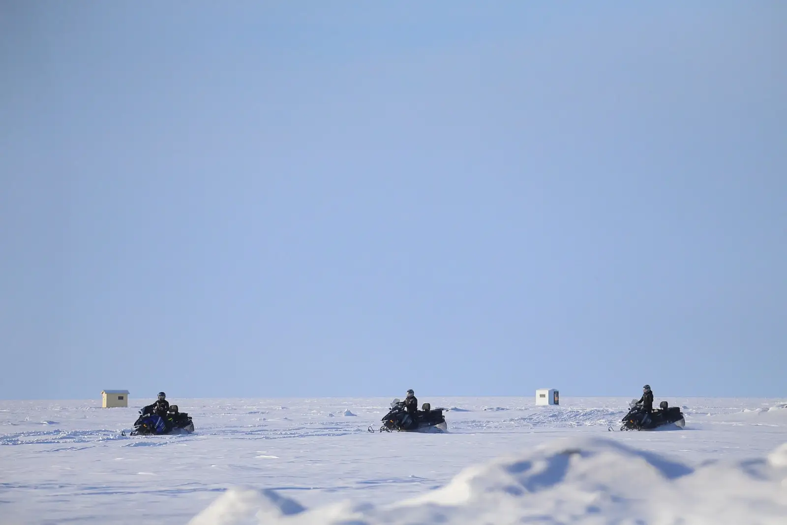 An expansive frozen Lac Saint-Jean with snowmobiles traversing its pristine icy surface under a clear winter sky.