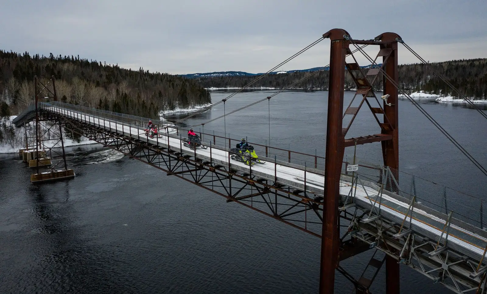 Vue aérienne d’un motoneigiste traversant un pont enneigé à Baie-Comeau.