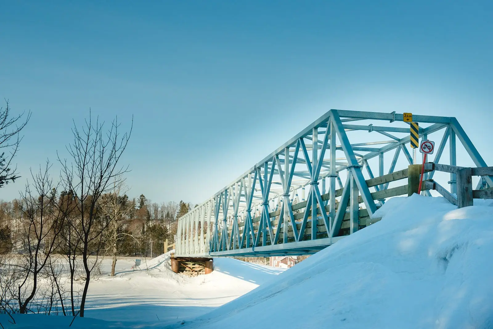 Un pont en acier bleu clair au-dessus d’un paysage enneigé, sous un ciel bleu clair par une journée hivernale ensoleillée.