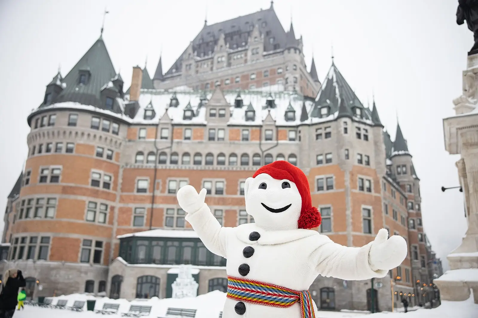 Bonhomme Carnaval, the mascot, standing in front of Château Frontenac, smiling and welcoming visitors on a snowy day in Québec City.