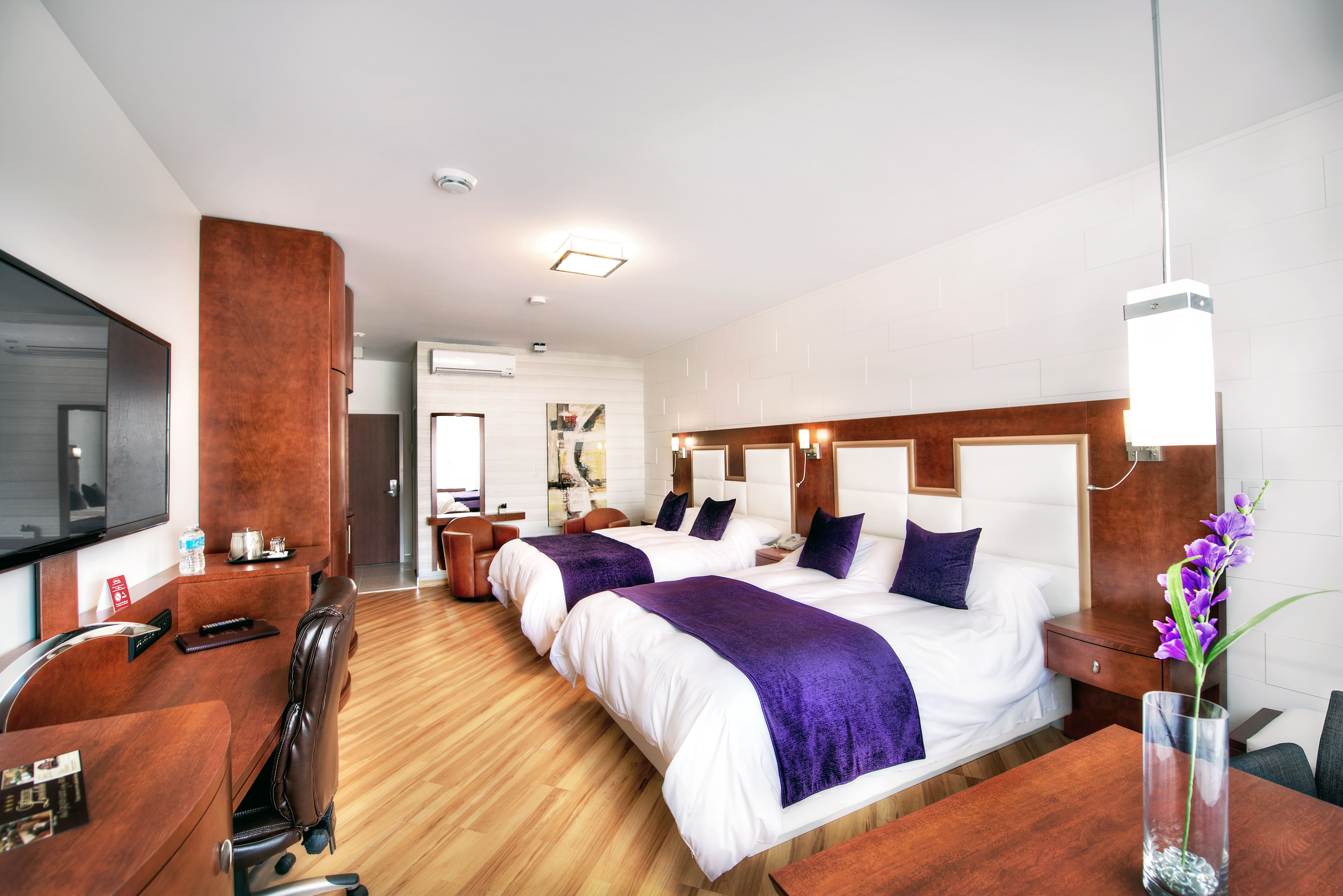  Interior of an elegant room at Les Suites Laviolette with two beds decorated with purple bedspreads, a wooden desk and modern details.